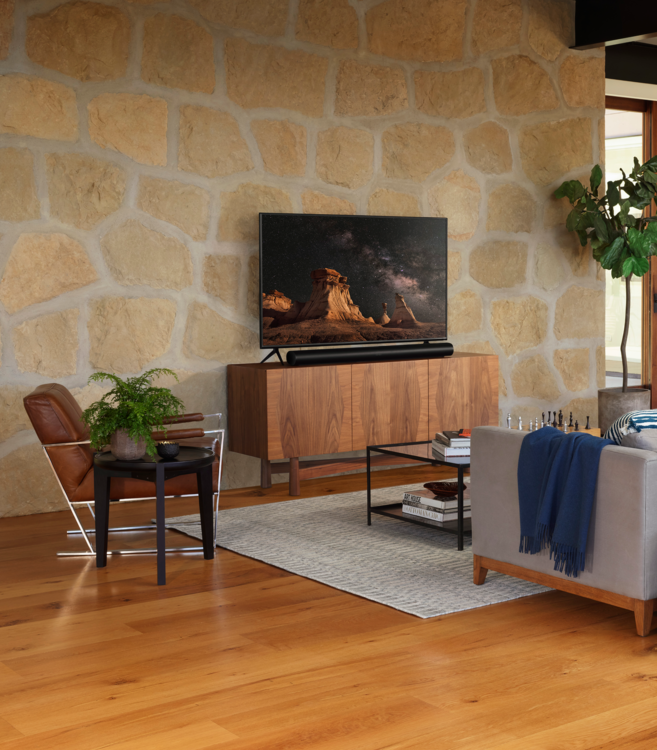 Woonkamer met tv, soundbar en kast. Een plant en een bank staan ​​op de voorgrond. Stenen muur als achtergrond.