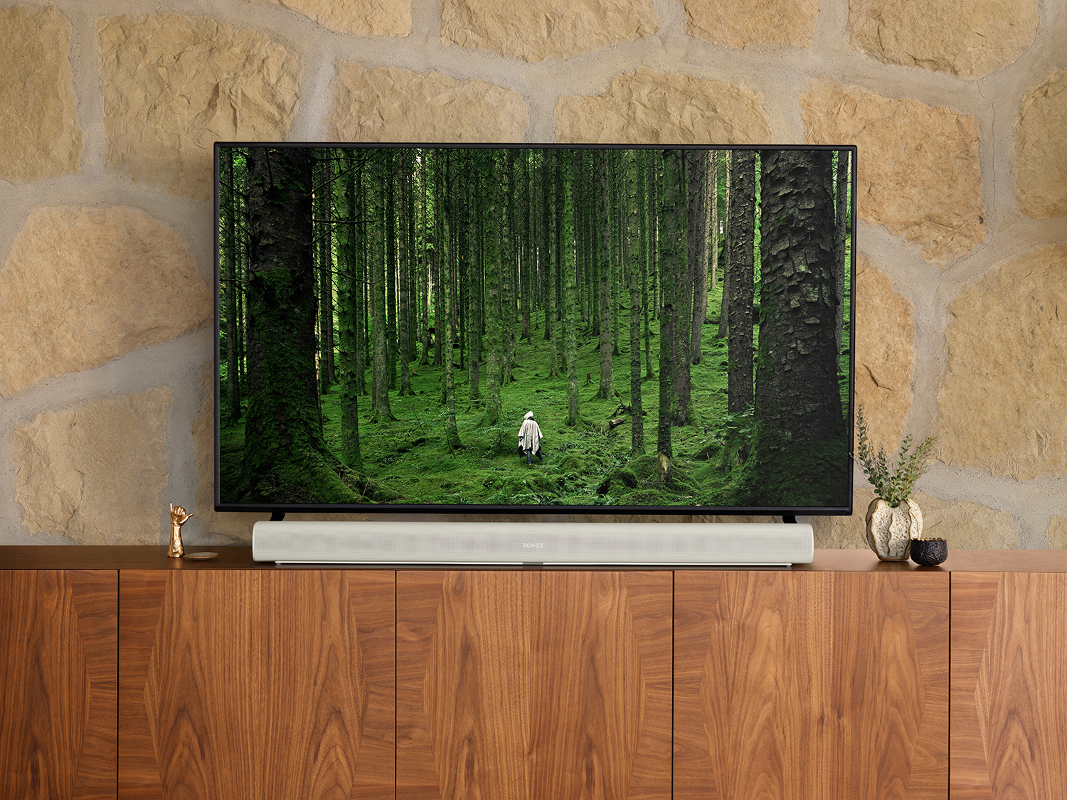 Tv-scherm toont een bosscène, boven een soundbar op een houten kast.