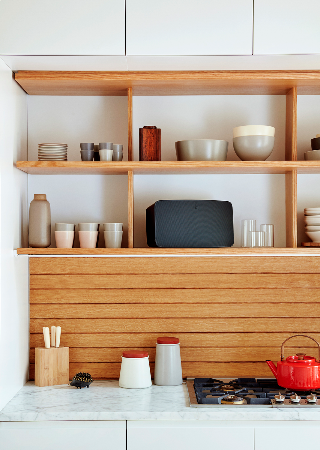Kitchen with wooden shelves, various items, and a red kettle on the stove.