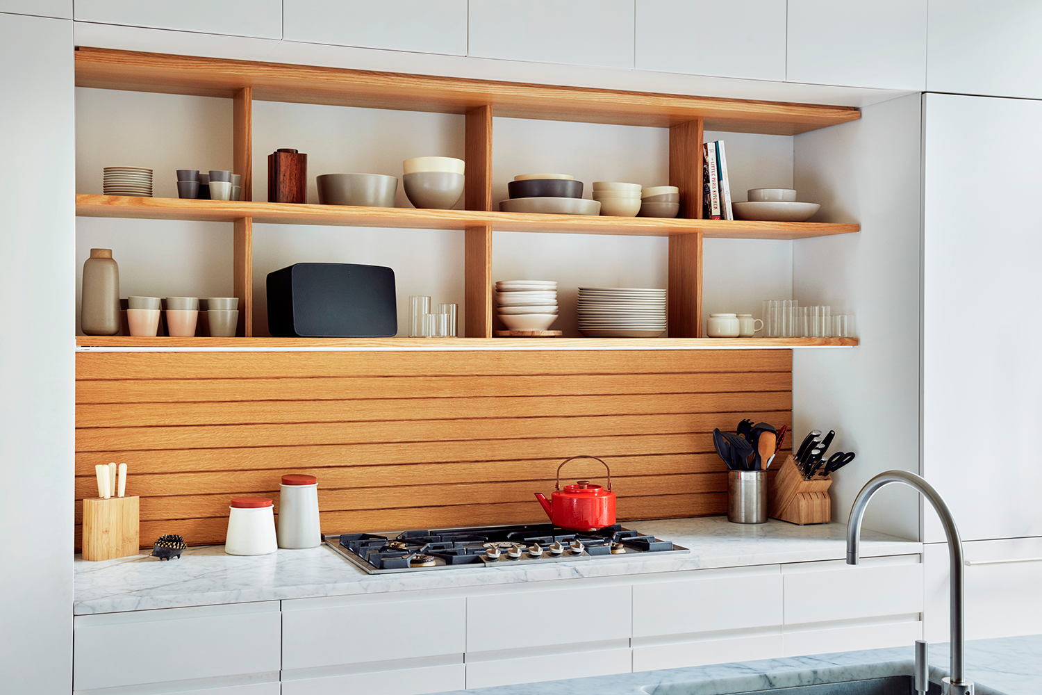 Kitchen with wooden shelves, various items, and a red kettle on the stove.