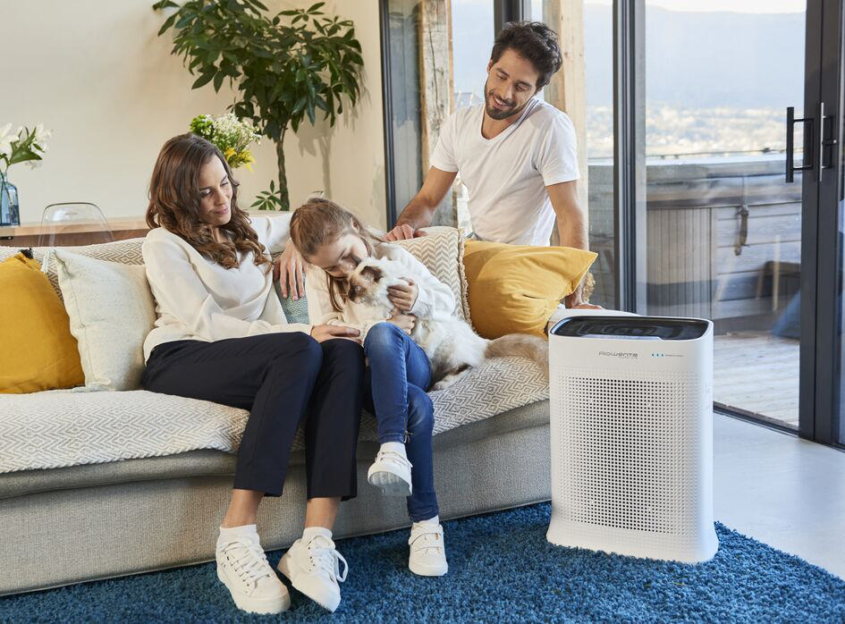 Eine Familie sitzt auf einer Couch, in der Nähe befindet sich ein Luftreiniger.