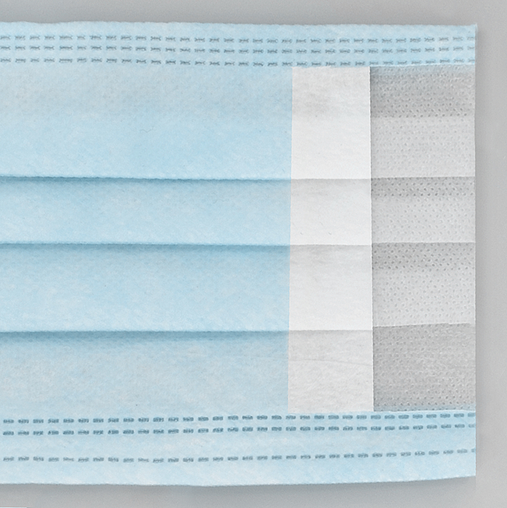 Nahaufnahme einer blauen OP-Maske. Sie ist gefaltet und zeigt verschiedene Schichten. Weißer Hintergrund.