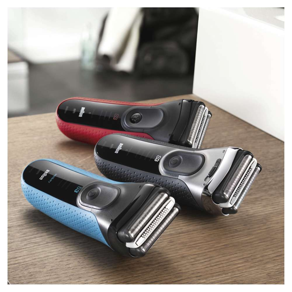 Tres afeitadoras eléctricas, roja, gris y azul. Están dispuestas sobre una superficie de madera.