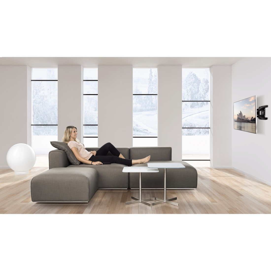 Frau, die sich auf einem grauen Sofa, einem weißen Tisch und einem Fernseher an der Wand in einem weißen Raum zurücklehnt.