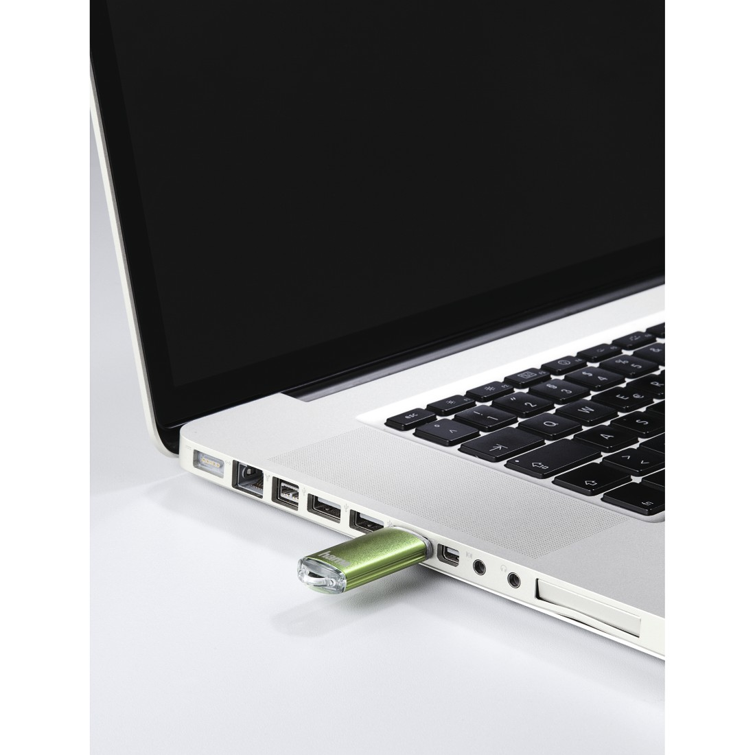 Laptop mit grünem USB-Stick, der seitlich eingesteckt ist, auf weißer Oberfläche.
