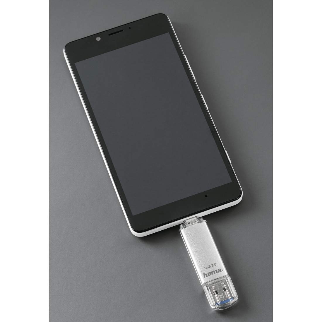 Smartphone mit USB-Stick verbunden. Telefon weiß-schwarz, Stick silber. Grauer Hintergrund.