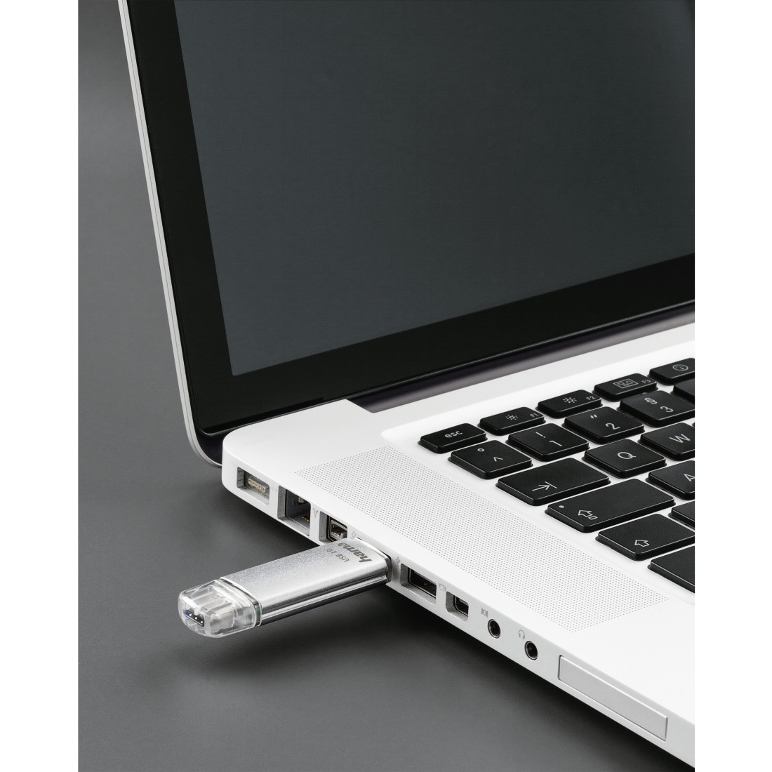 Ein silberner USB-Stick, der in einen Laptop gesteckt ist. Der Laptop befindet sich auf einer grauen Oberfläche.