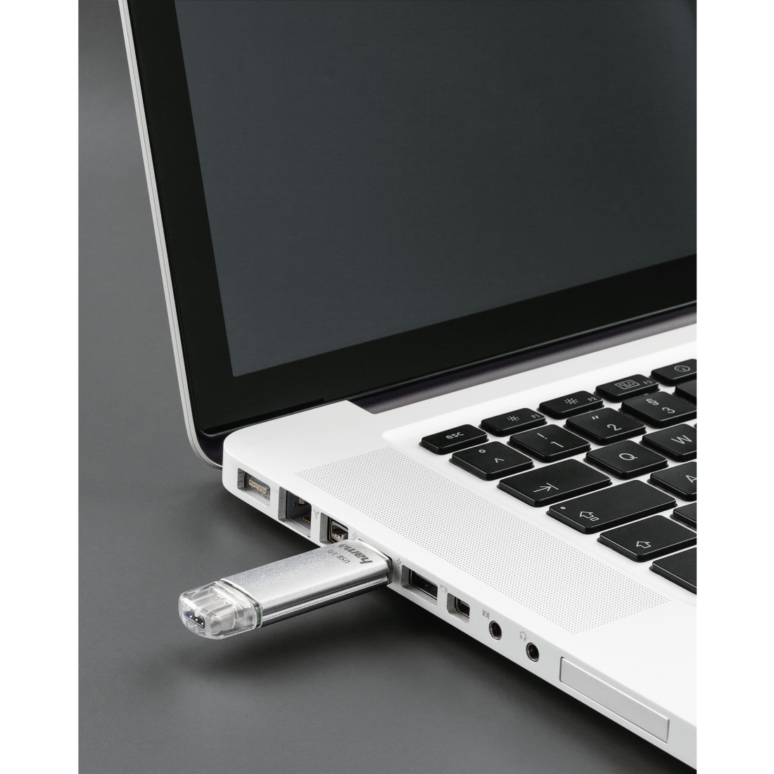Ein silberner USB-Stick, der in einen silbernen Laptop gesteckt wird, auf dunkler Oberfläche.
