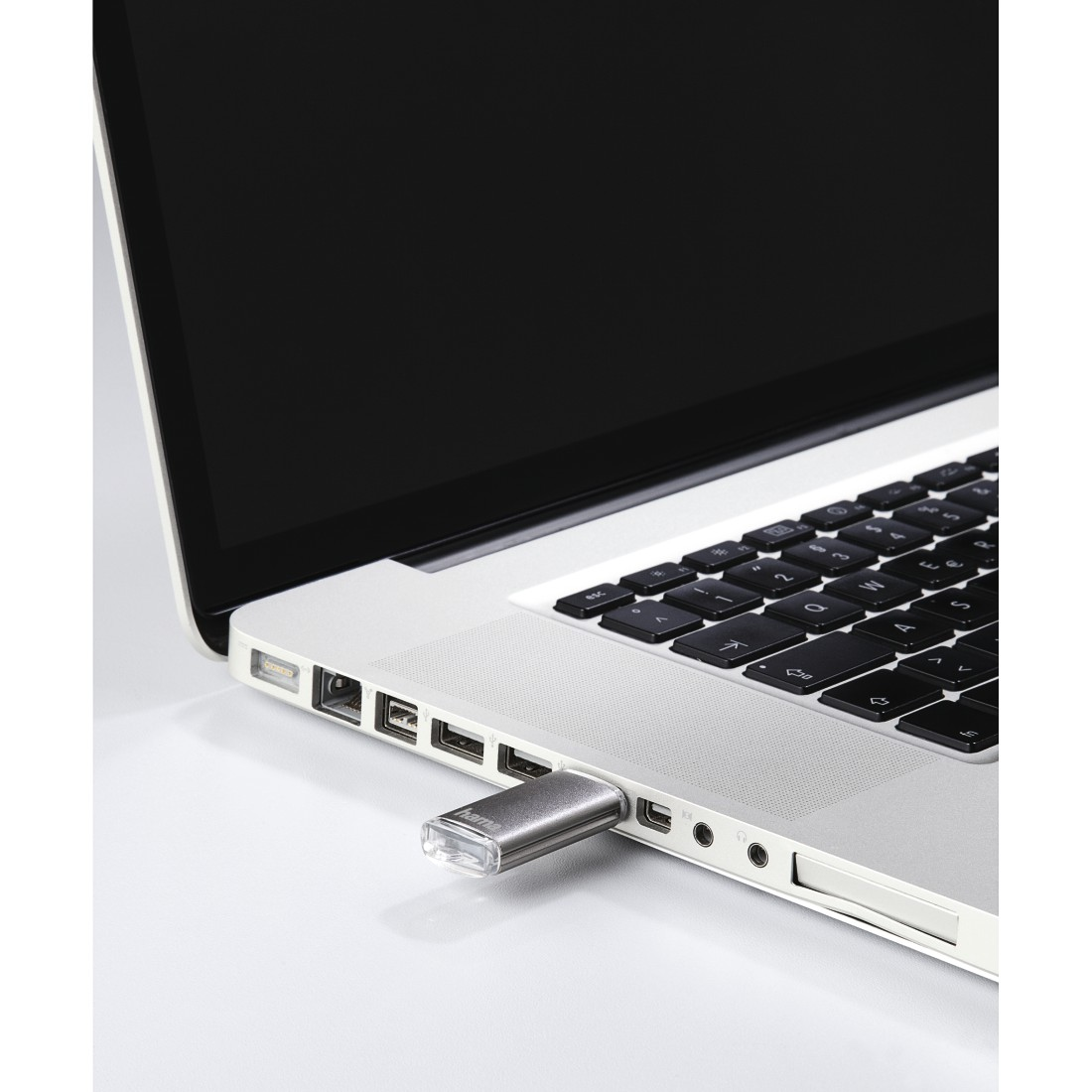 Silberner USB-Stick in einen Laptop gesteckt, neben Anschlüssen. Der Laptop ist geöffnet.