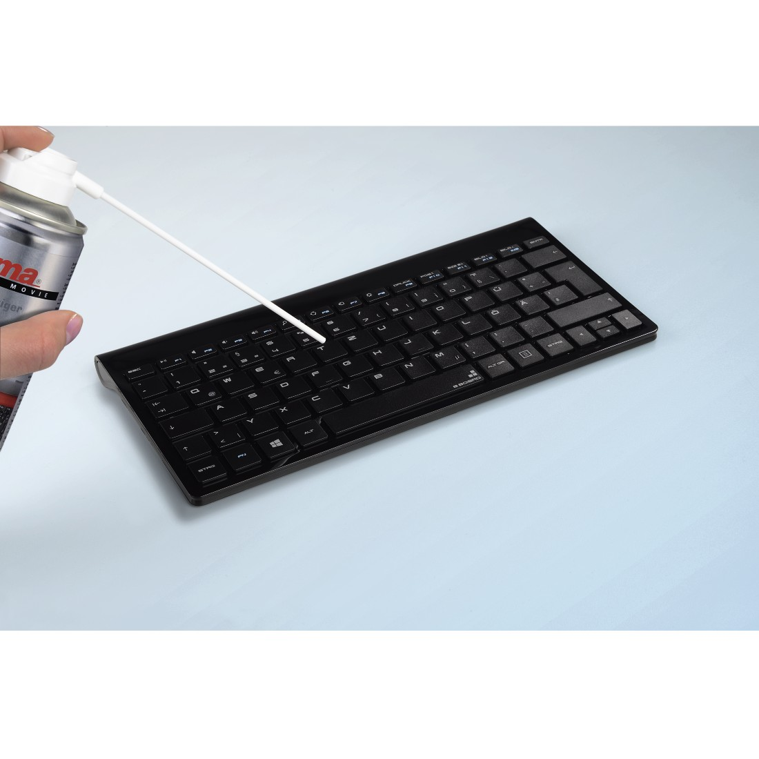 Eine Hand sprüht eine Tastatur mit einem Reiniger ein. Blauer Hintergrund.
