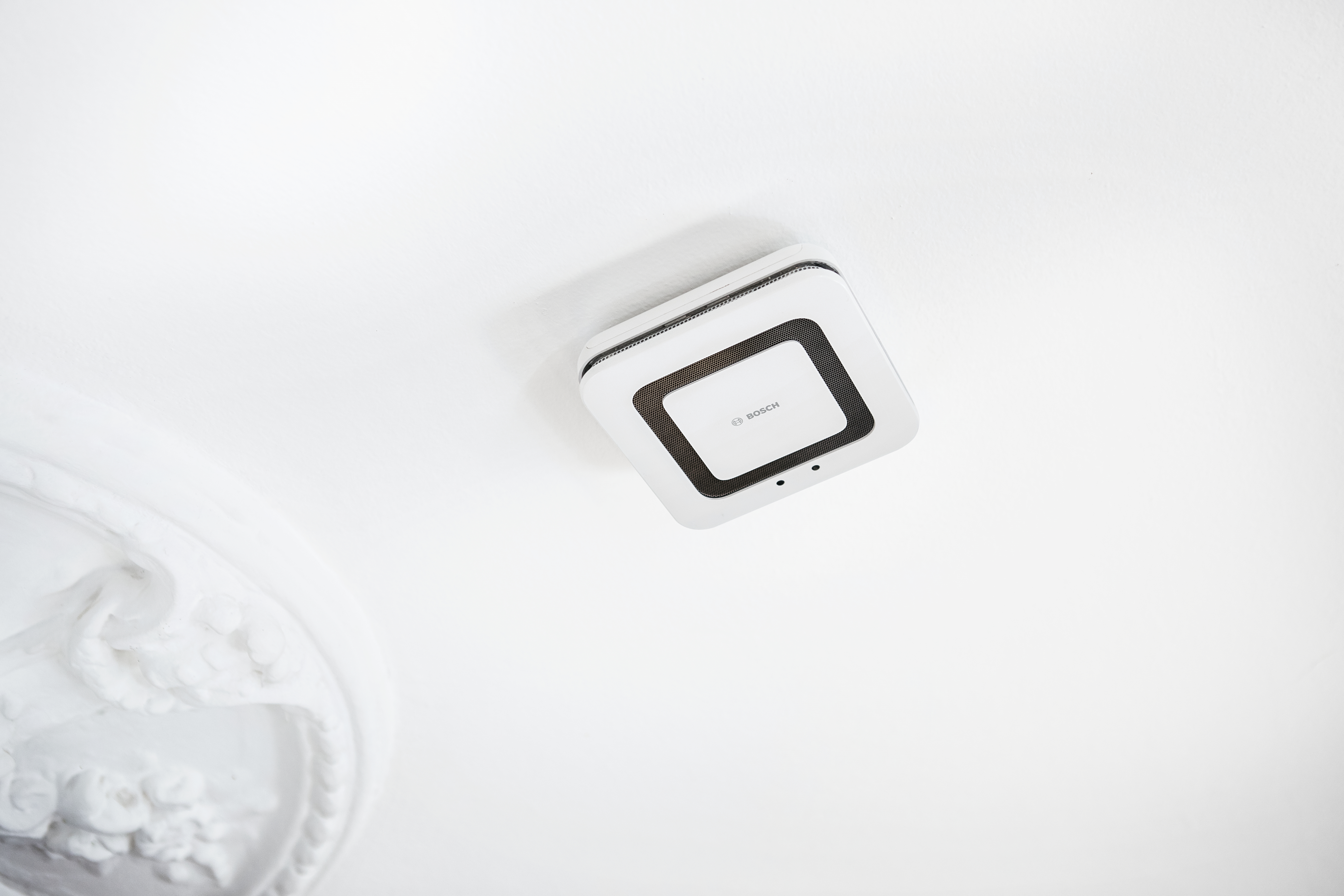 Ein weißes quadratisches Gerät an einer weißen Decke befestigt. Das Gerät hat das Bosch-Logo. Winkelschuss.