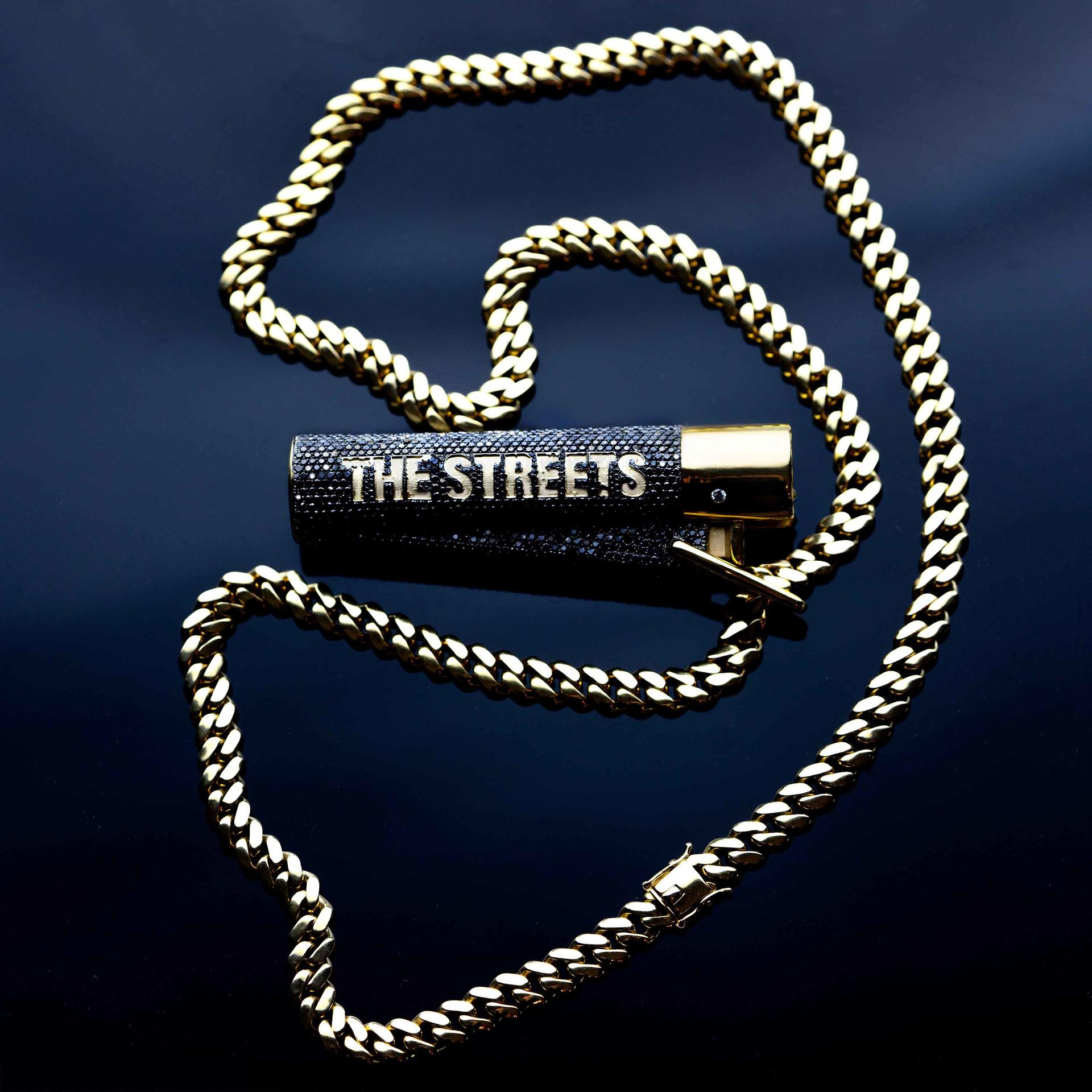 Gouden ketting en een zwarte aansteker met diamanten en de tekst 'THE STREETS'.