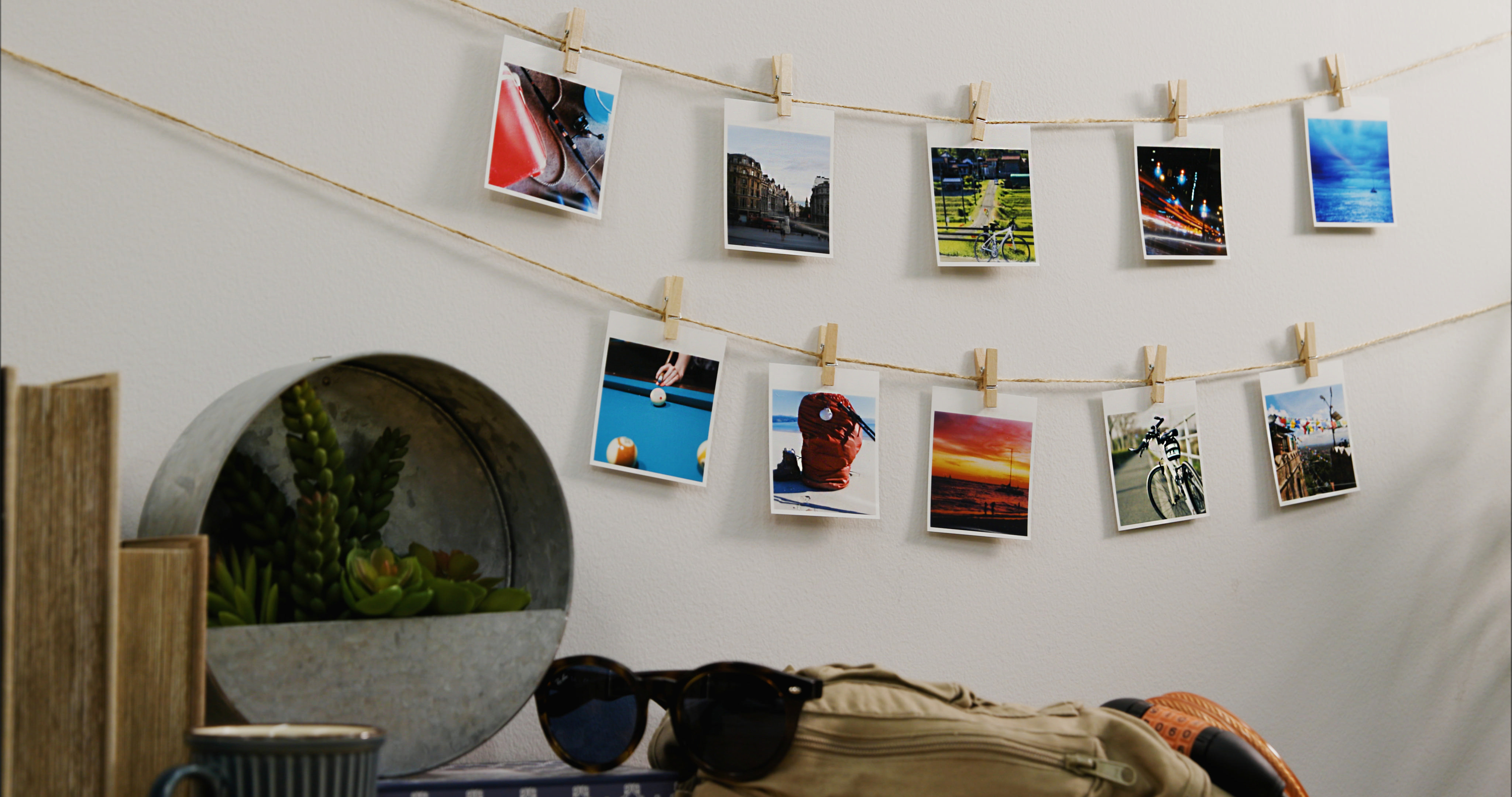Fotos hängen an einer Schnur mit Wäscheklammern. Ein Tisch mit Sonnenbrille, Tasche und Deko im Vordergrund.