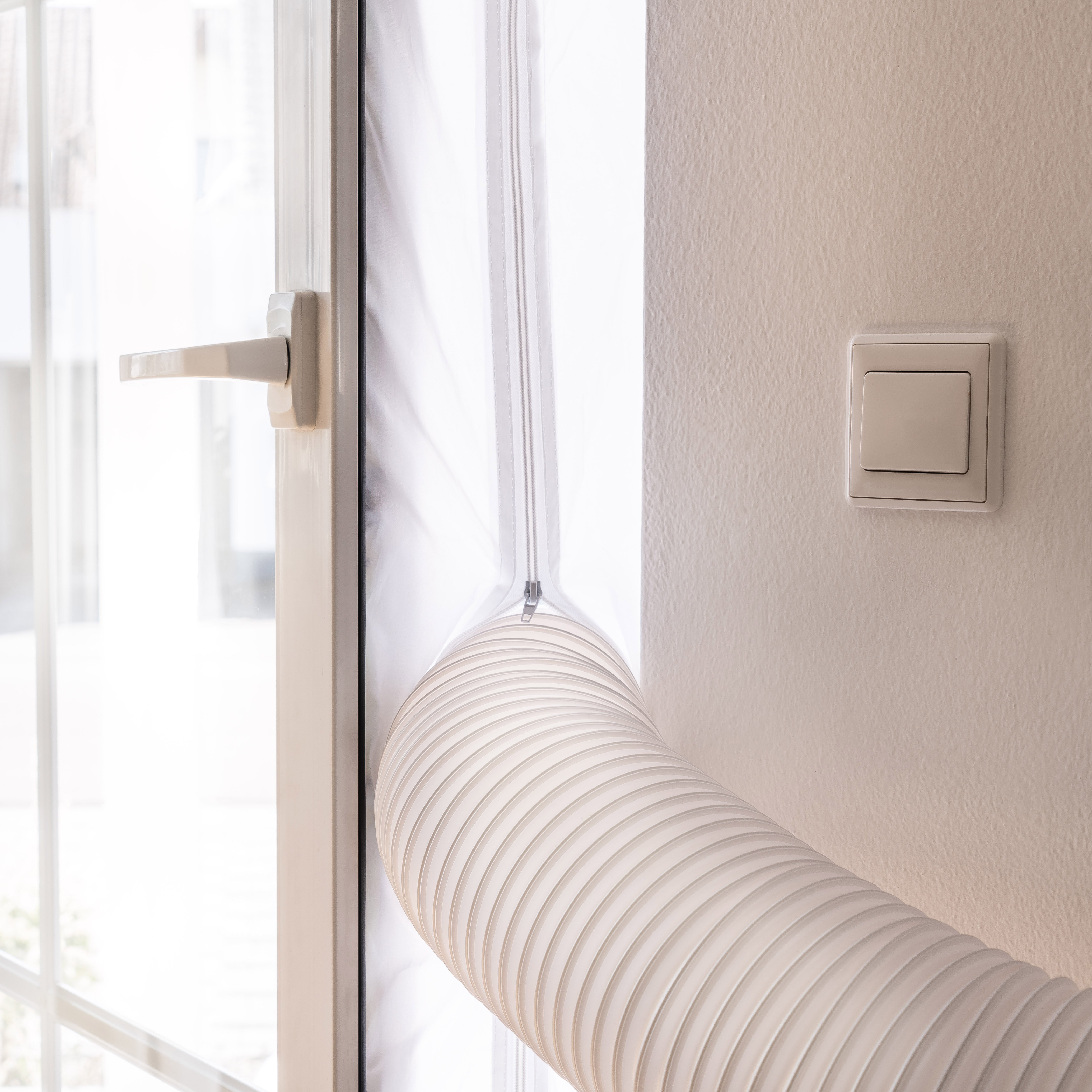 Ein weißer Klimaanlagenschlauch, der mit einem Fenster verbunden ist, mit weißer Wand und Lichtschalter.