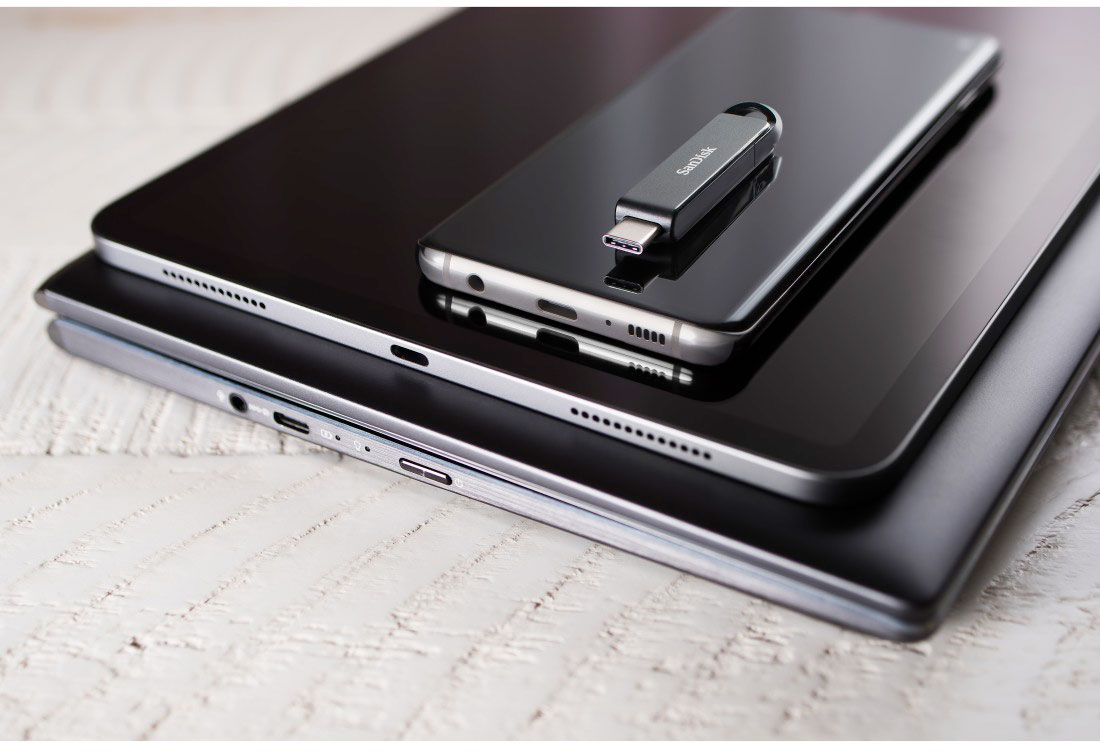 Tablets, phone, and USB drive on a light wooden surface, creating a tech arrangement.