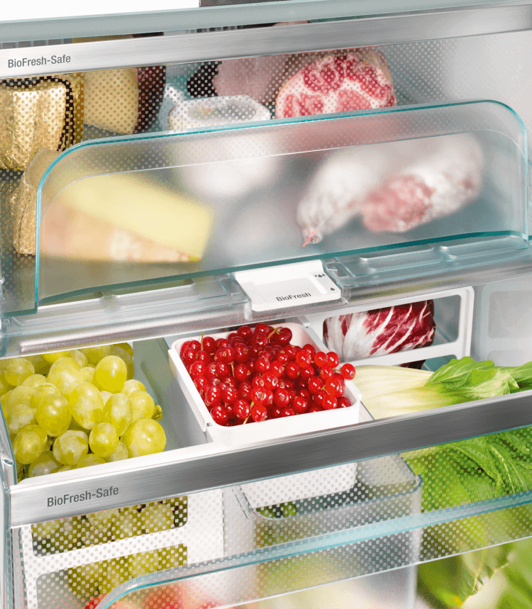 Refrigerator interior with fresh produce, including grapes, red currants, and cheese.