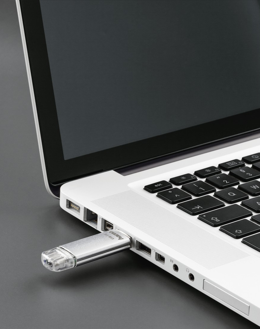 Ein silberner USB-Stick, der in einen weißen Laptop gesteckt wird.