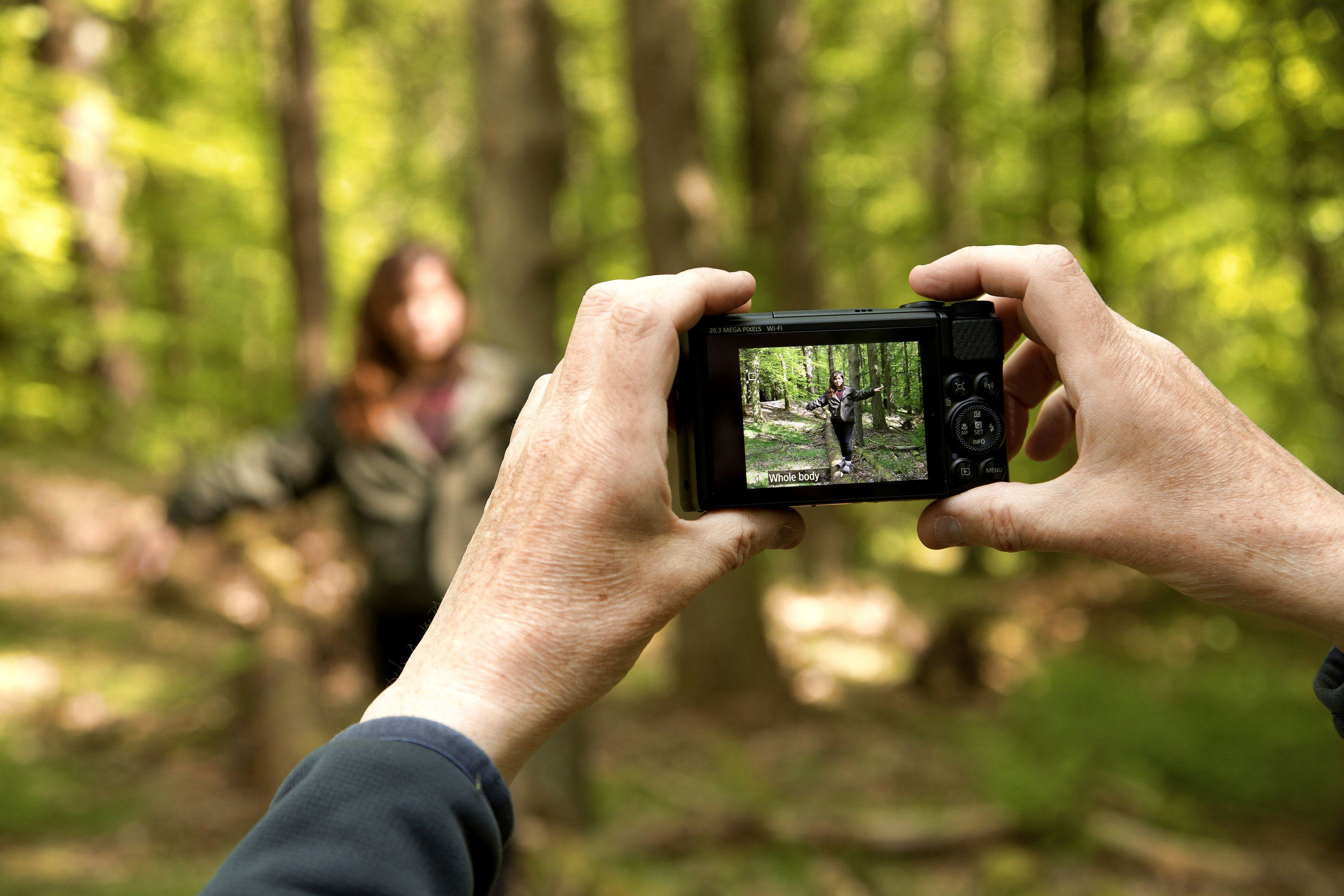 Person fotografiert eine Frau in einem Wald.