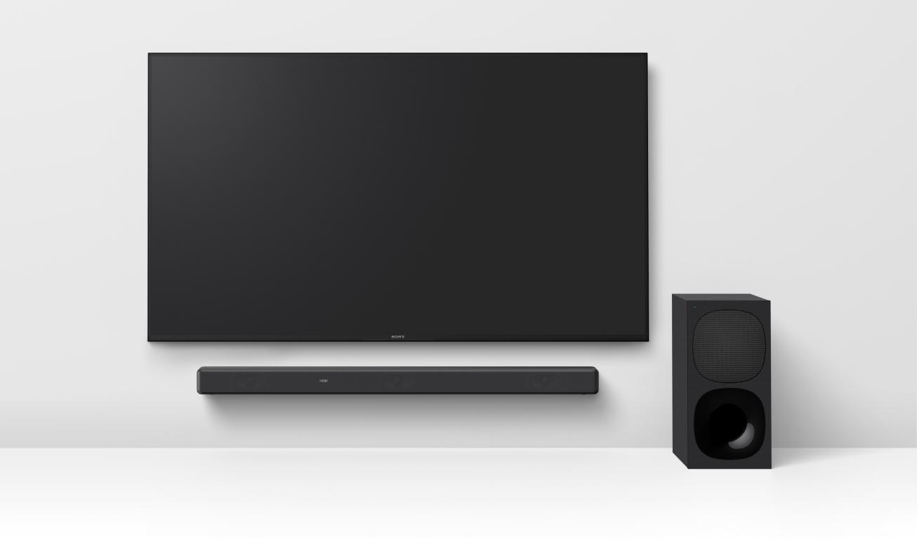 Televisor negro, barra de sonido y subwoofer sobre pared blanca.