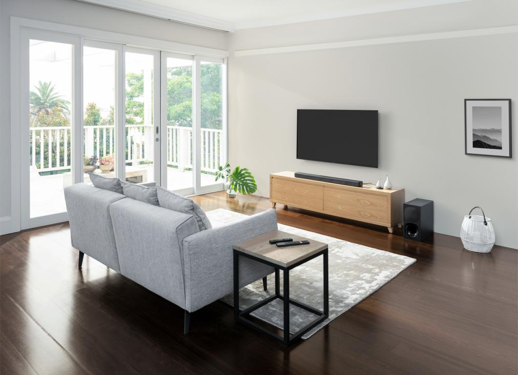 Una sala de estar con sofá, TV, barra de sonido, alfombra, mesa auxiliar y vista al exterior.
