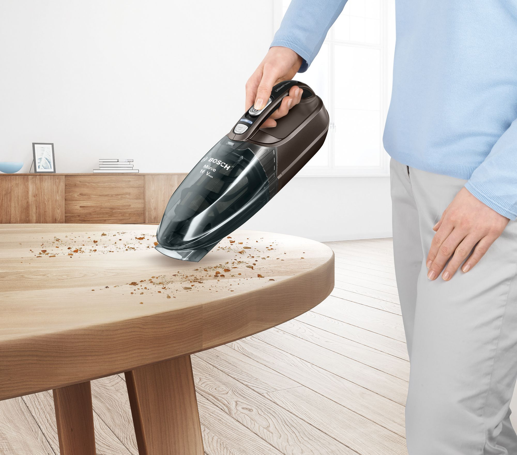 A person using a black and brown handheld vacuum cleaner on a wooden table.