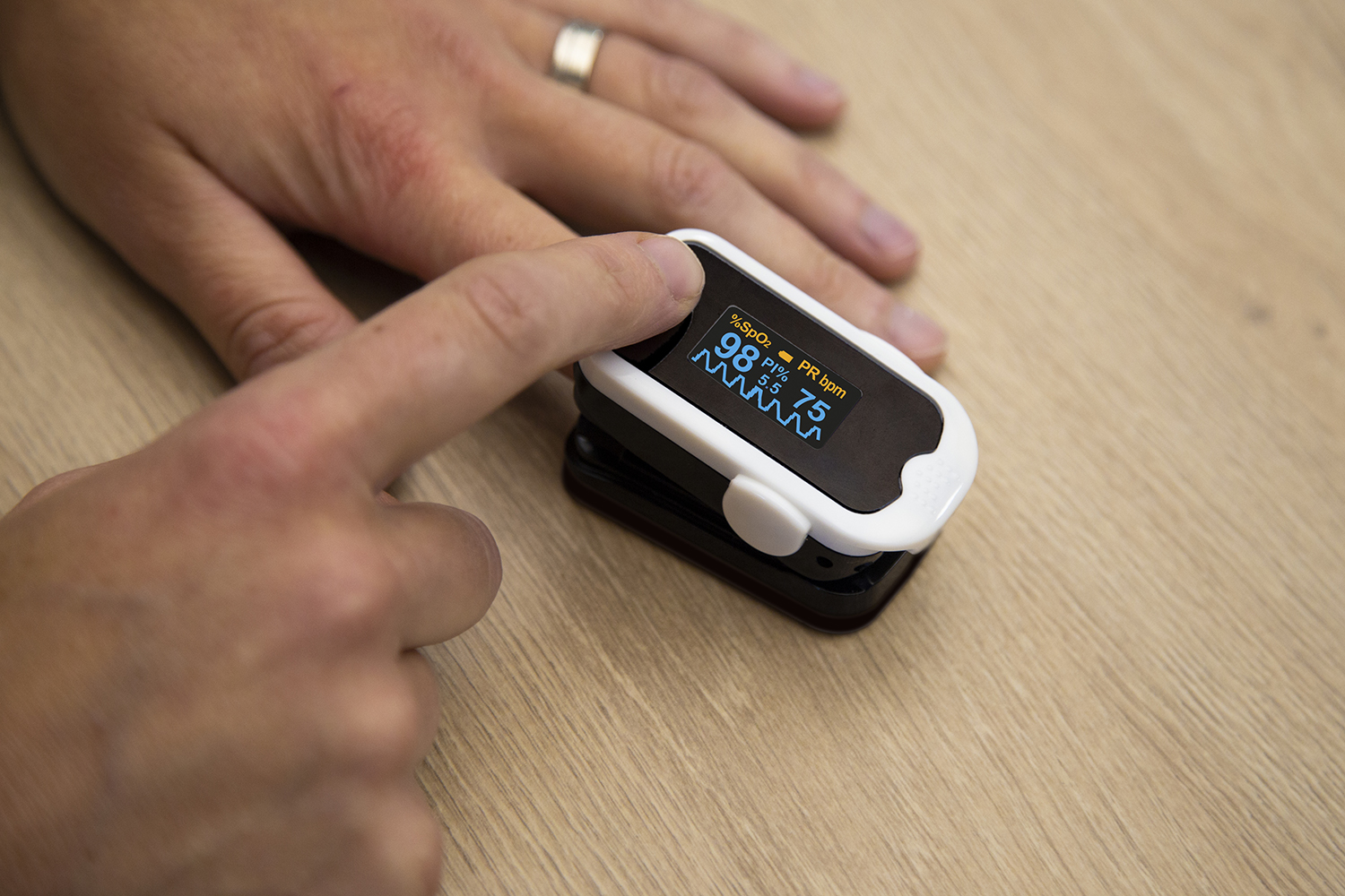 De vinger van een persoon zit in een pulsoximeter. De oximeter geeft zuurstof en polsslag weer.