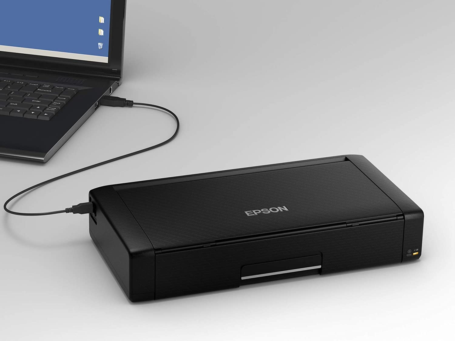 Impresora Epson negra conectada a una laptop por cable USB.