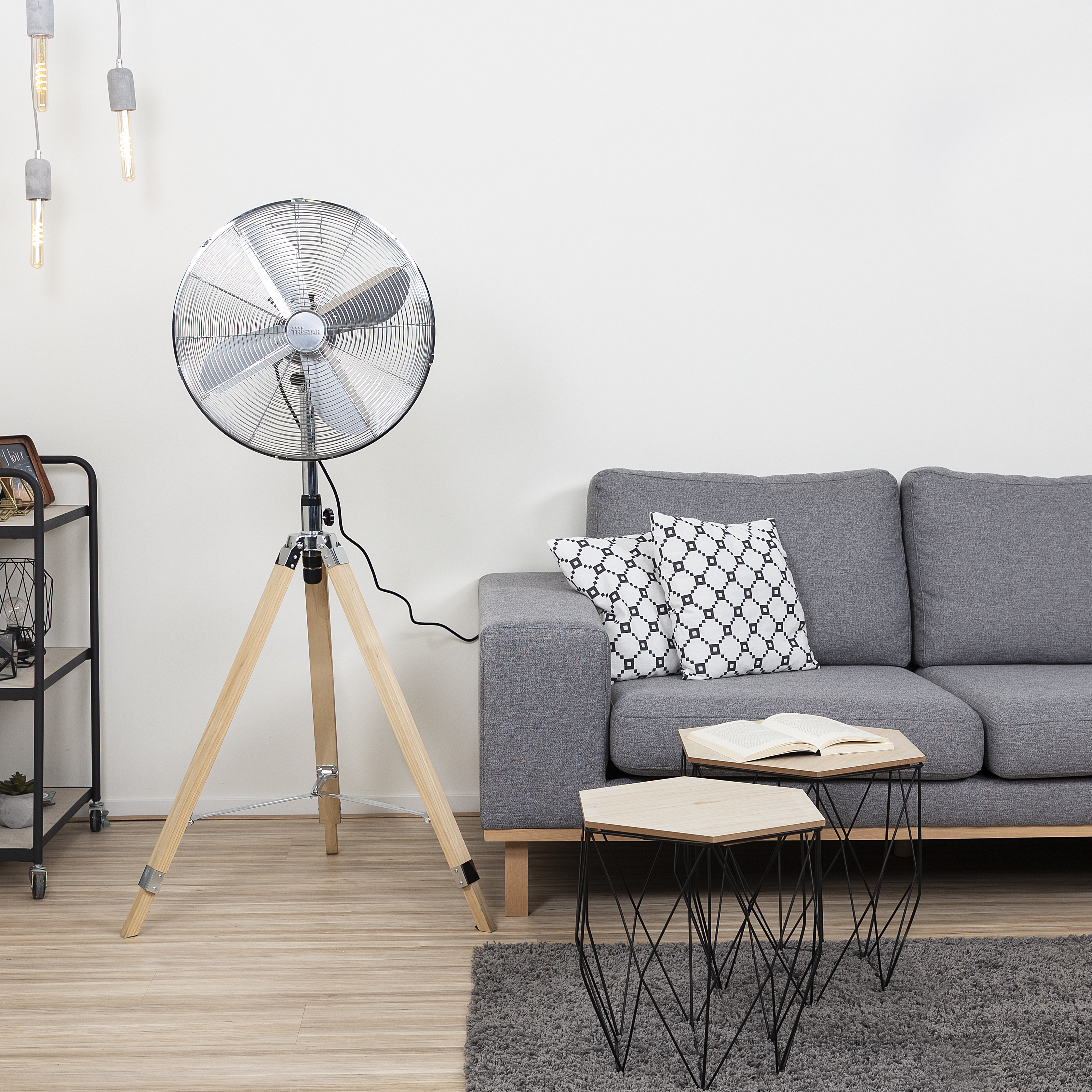 Ein Raum mit einem Standventilator, einem Sofa und Beistelltischen. Es ist ein Wohnzimmer.