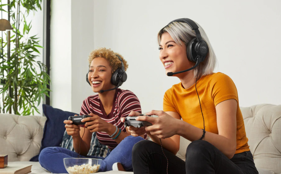 Two smiling women with headsets play a game, one holding a controller.