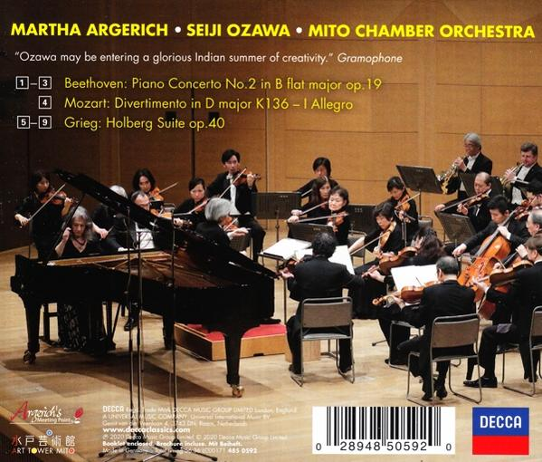 Orkest dat optreedt op het podium, met een piano vooraan en een cd-hoes op de achtergrond.