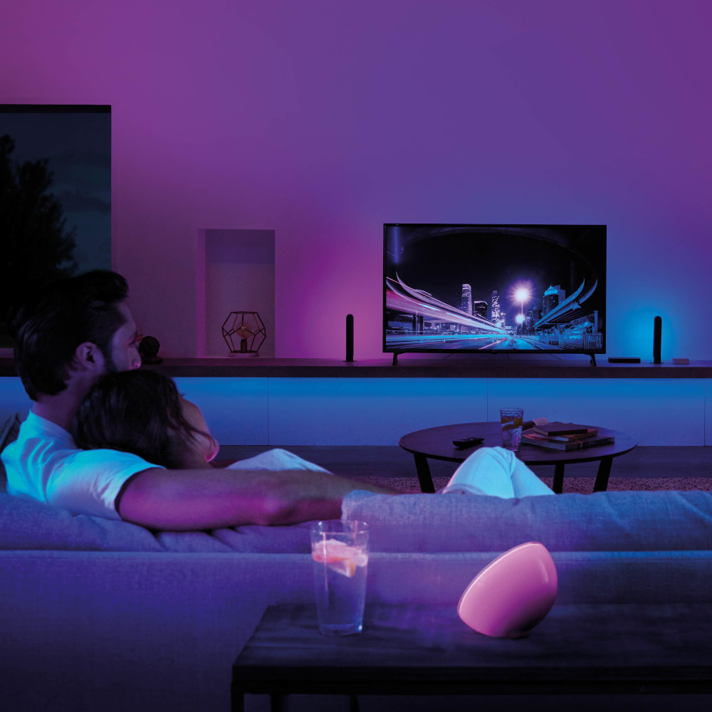 Koppel op een bank tv aan het kijken, met een tafel en een lamp op de voorgrond.