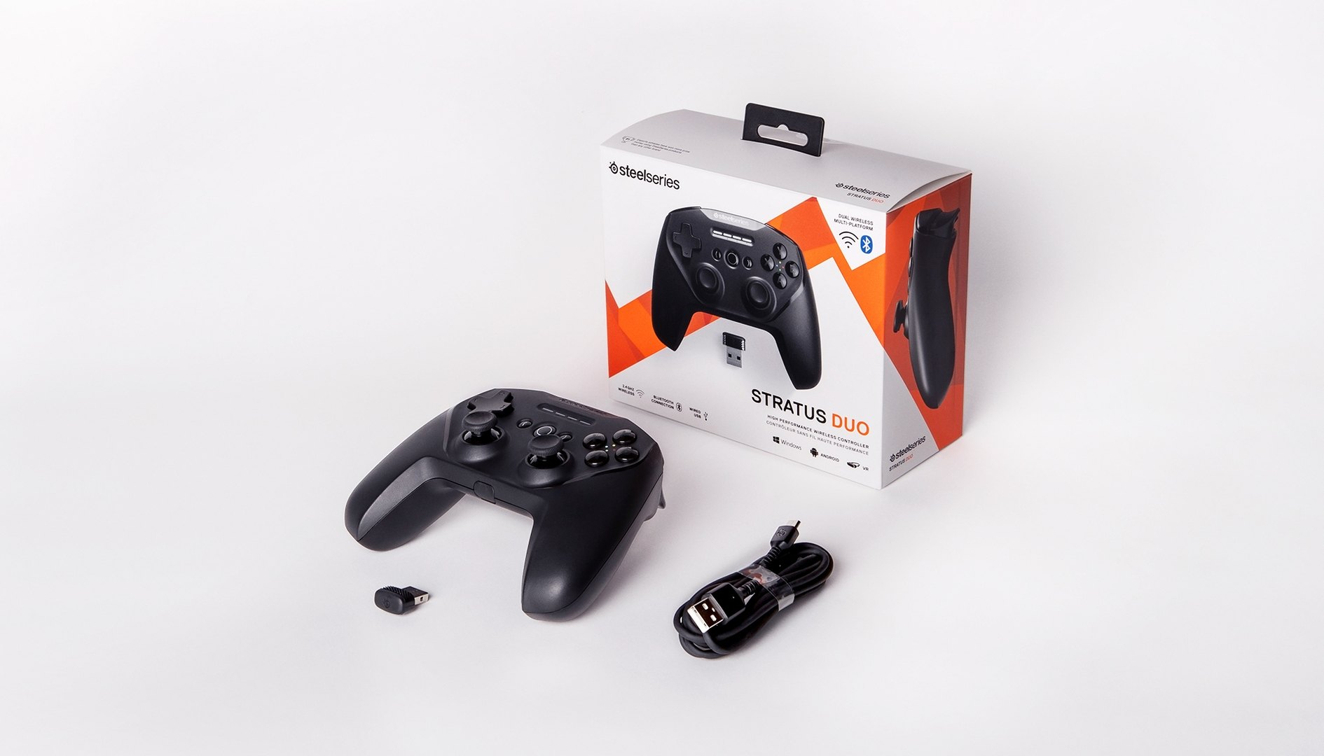 Fekete SteelSeries Stratus Duo vezérlő, doboz, USB kábel és vezeték nélküli adapter fehér alapon.