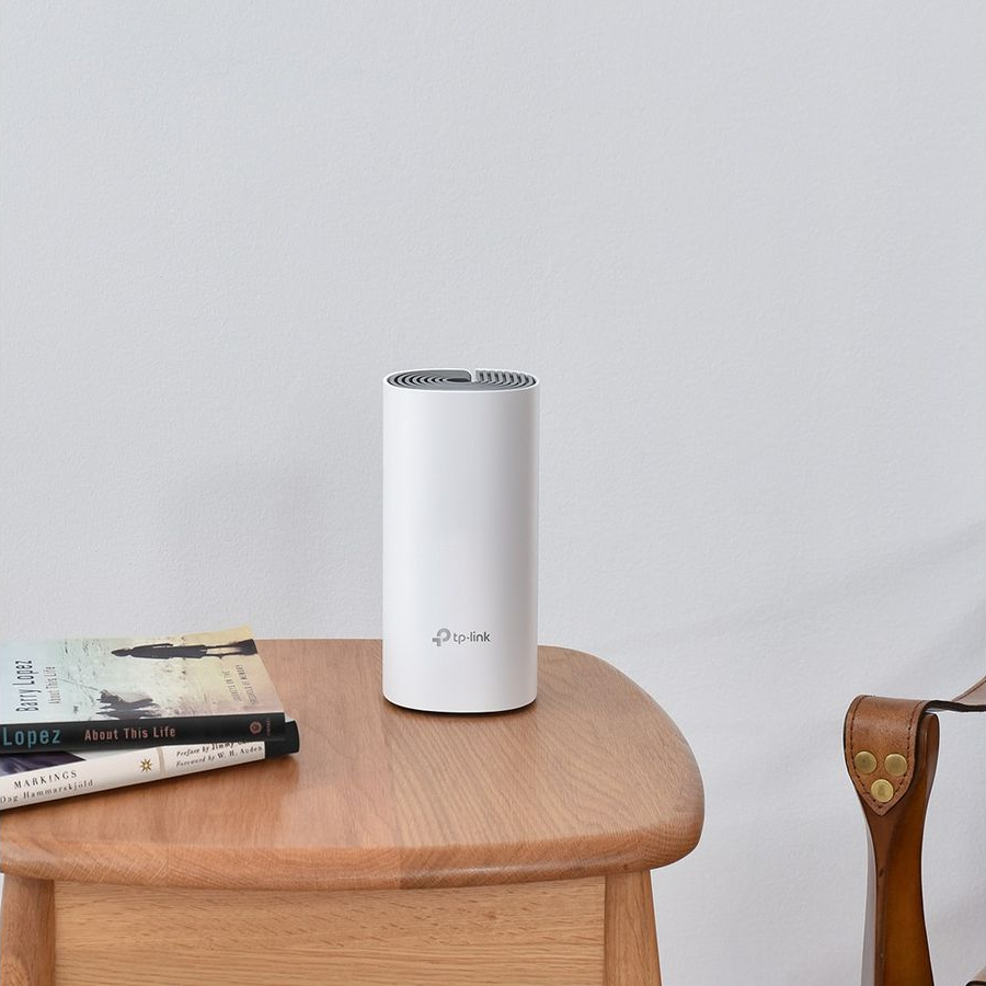Routeur TP-Link blanc cylindrique sur table en bois. Livres et chaise en arrière-plan.
