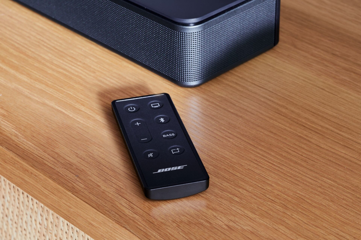Schwarze Bose-Fernbedienung auf einem Holztisch, mit einer schwarzen Soundbar im Hintergrund.