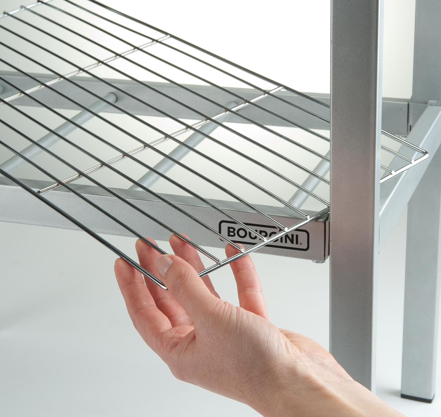 A hand reaching for a chrome metal shelf in a silver frame, close up.