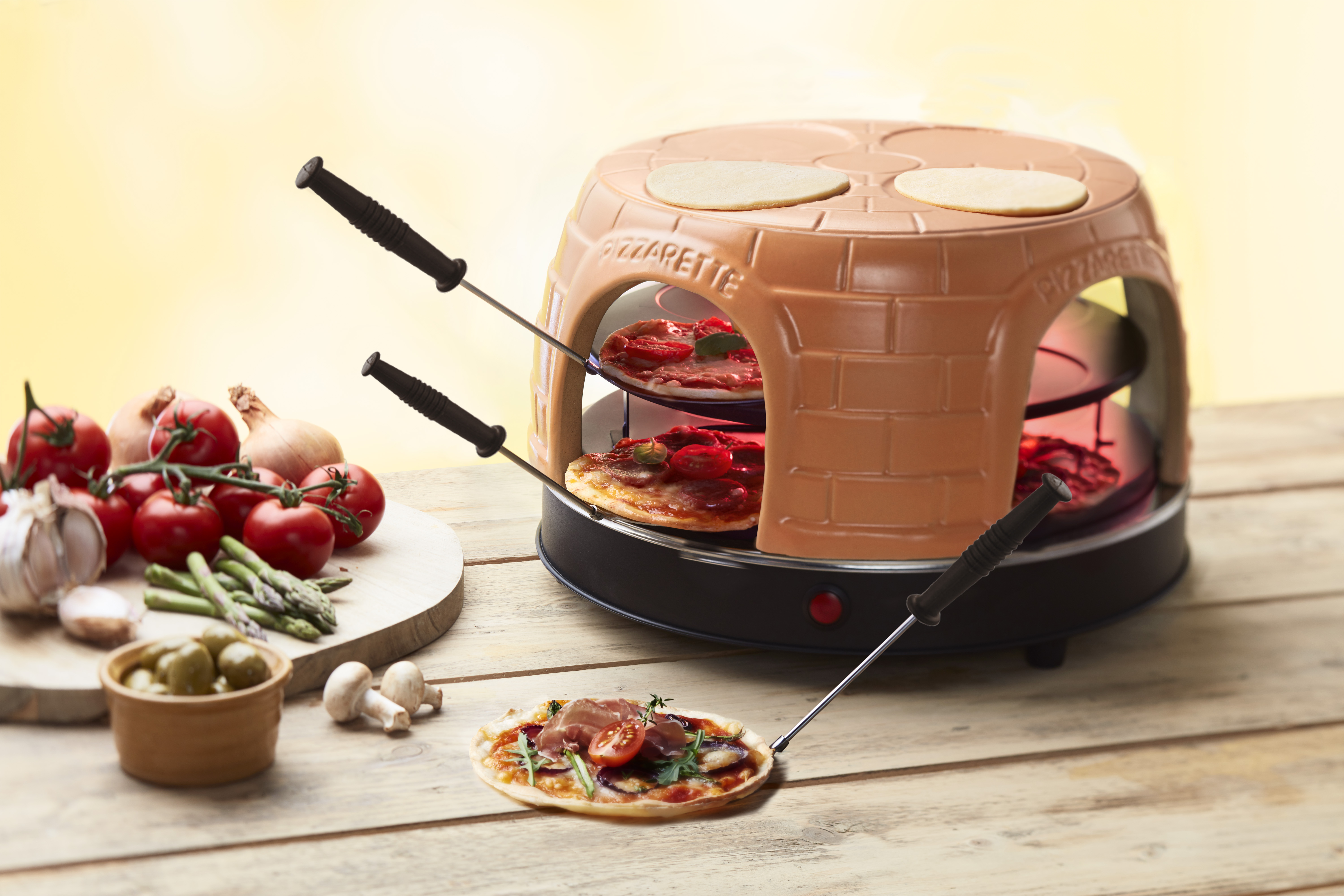 Pizzaofen mit Pizzen im Inneren. Gemüse, Oliven und Pilze sind auf der Seite.