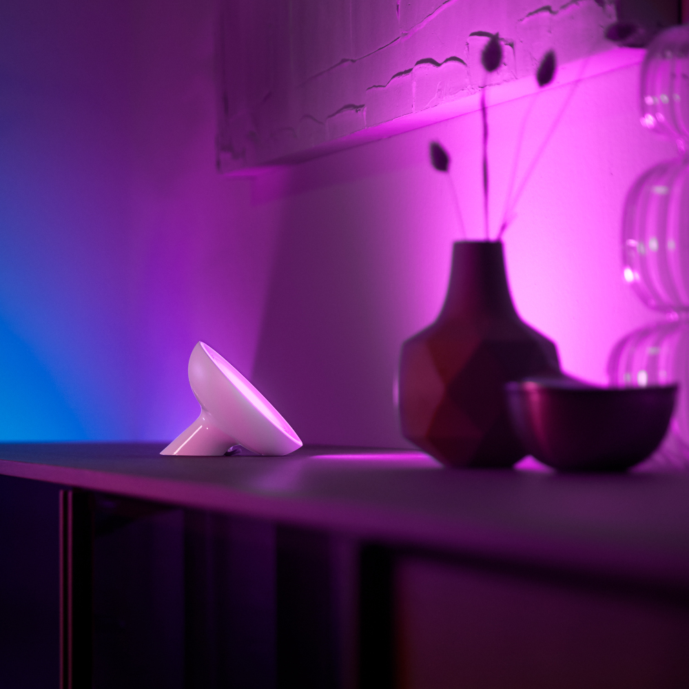 White lamp on a table, purple and blue ambient lighting, with a vase and a bowl.
