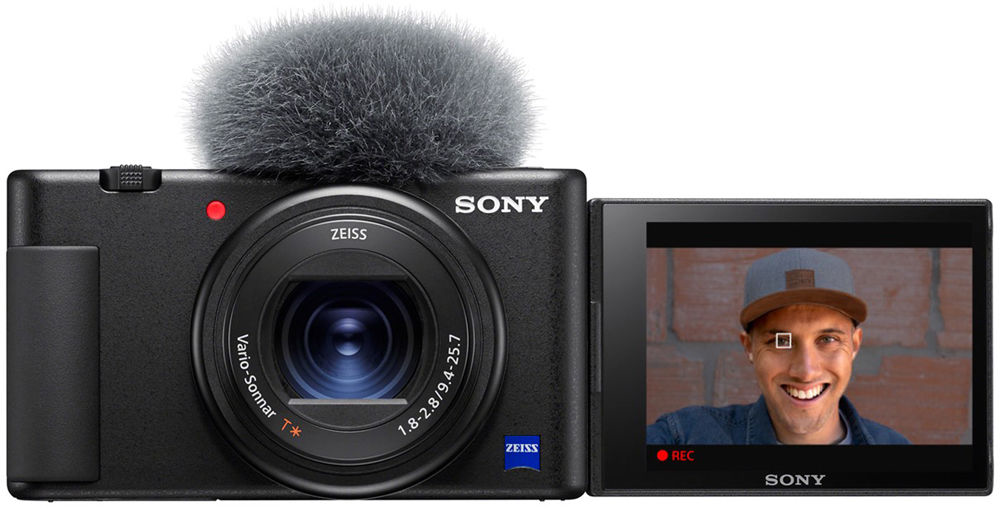 Fekete Sony kamera szőrös mikrofonnal, egy mosolygó férfit mutató képernyővel.