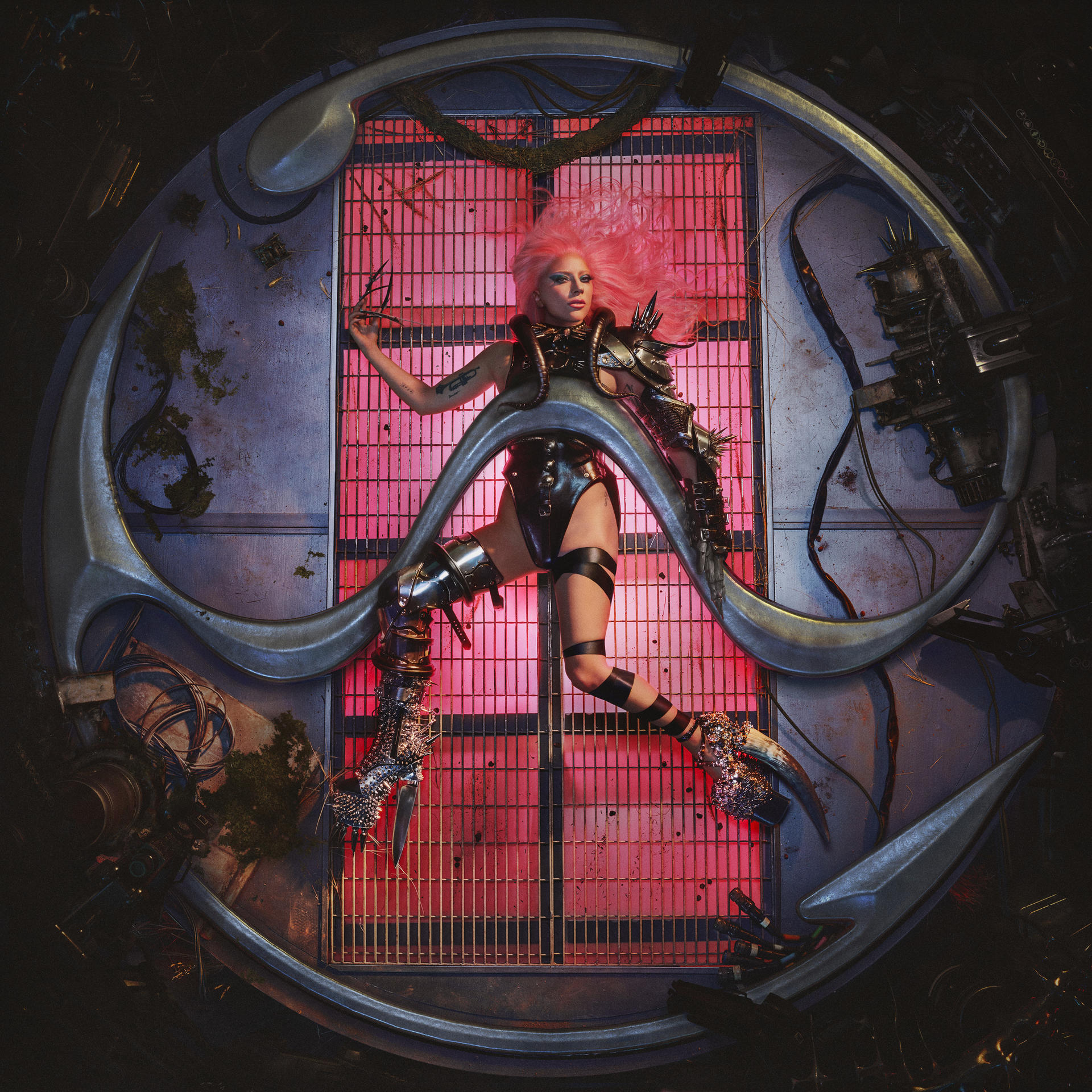 Lady Gaga in futuristischem Outfit, umgeben von Metallstruktur mit pinkem Hintergrund.
