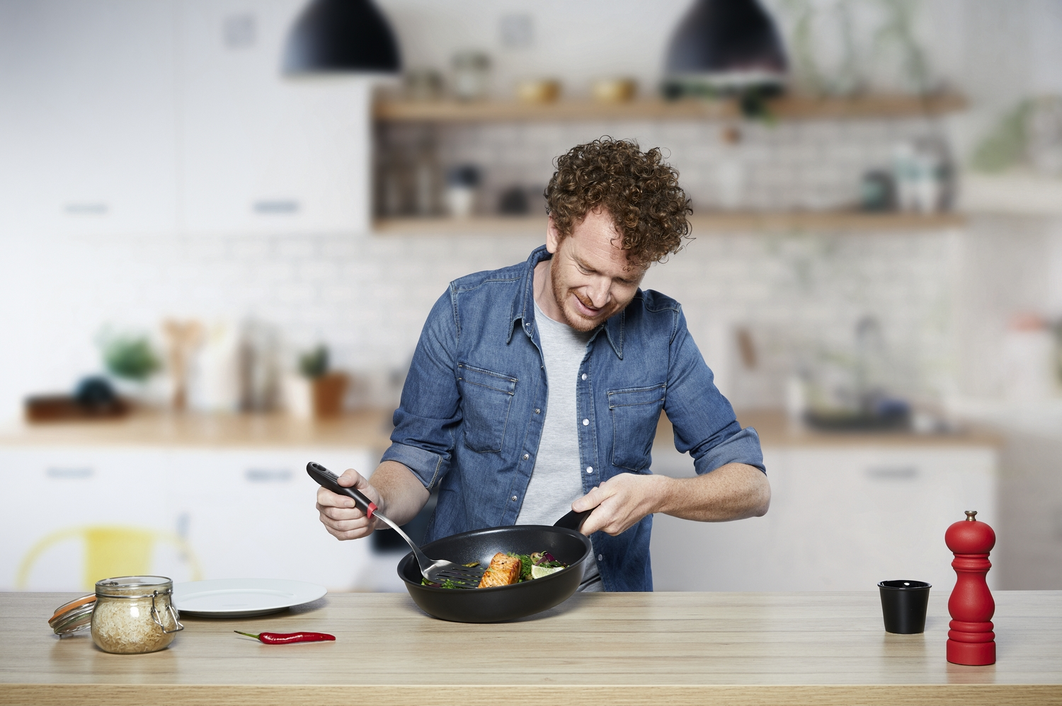 Un hombre cocinando en una cocina, usando una sartén y espátula. Está sonriendo.