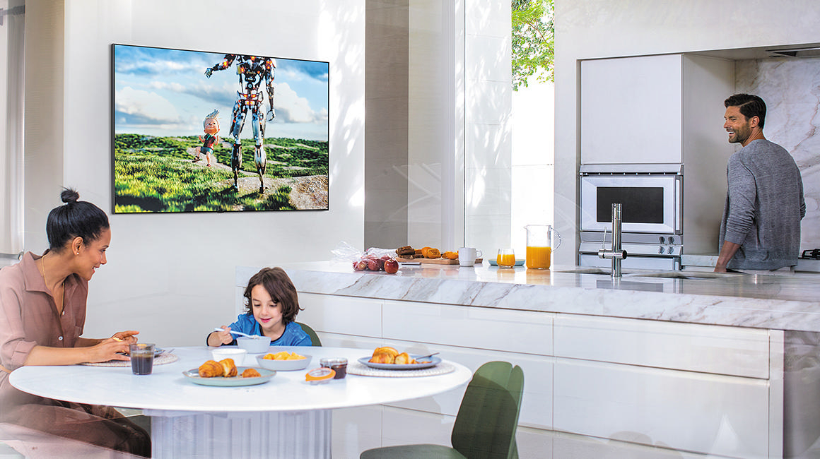 Frau und Junge frühstücken am Fernseher. Mann in der Küche.