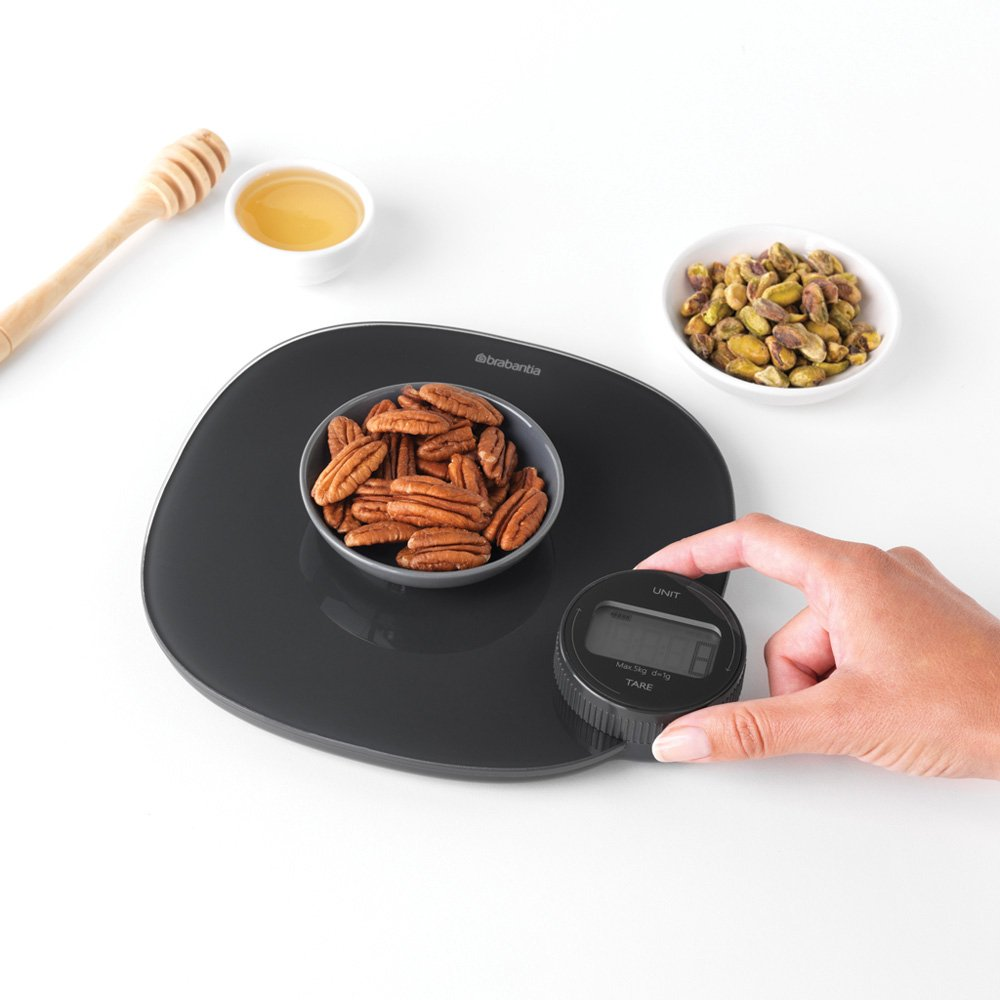 Une balance noire avec un bol de noix de pécan, de miel et de pistaches.