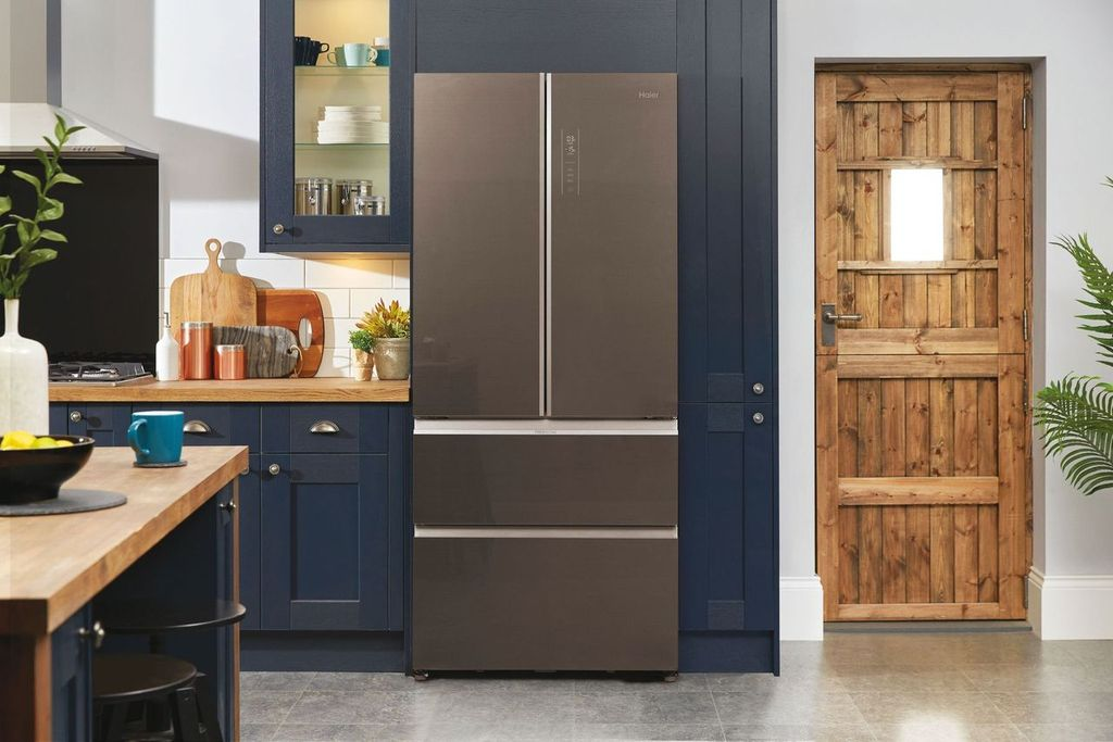 Cocina con una nevera Haier, puerta de madera y armarios azules, con una encimera de madera.