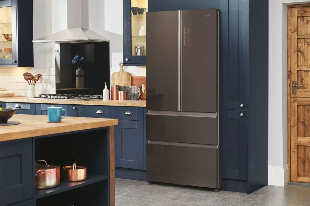 Un refrigerador Haier marrón oscuro en una cocina. La cocina tiene gabinetes azul oscuro, encimera de madera y acero inoxidable.