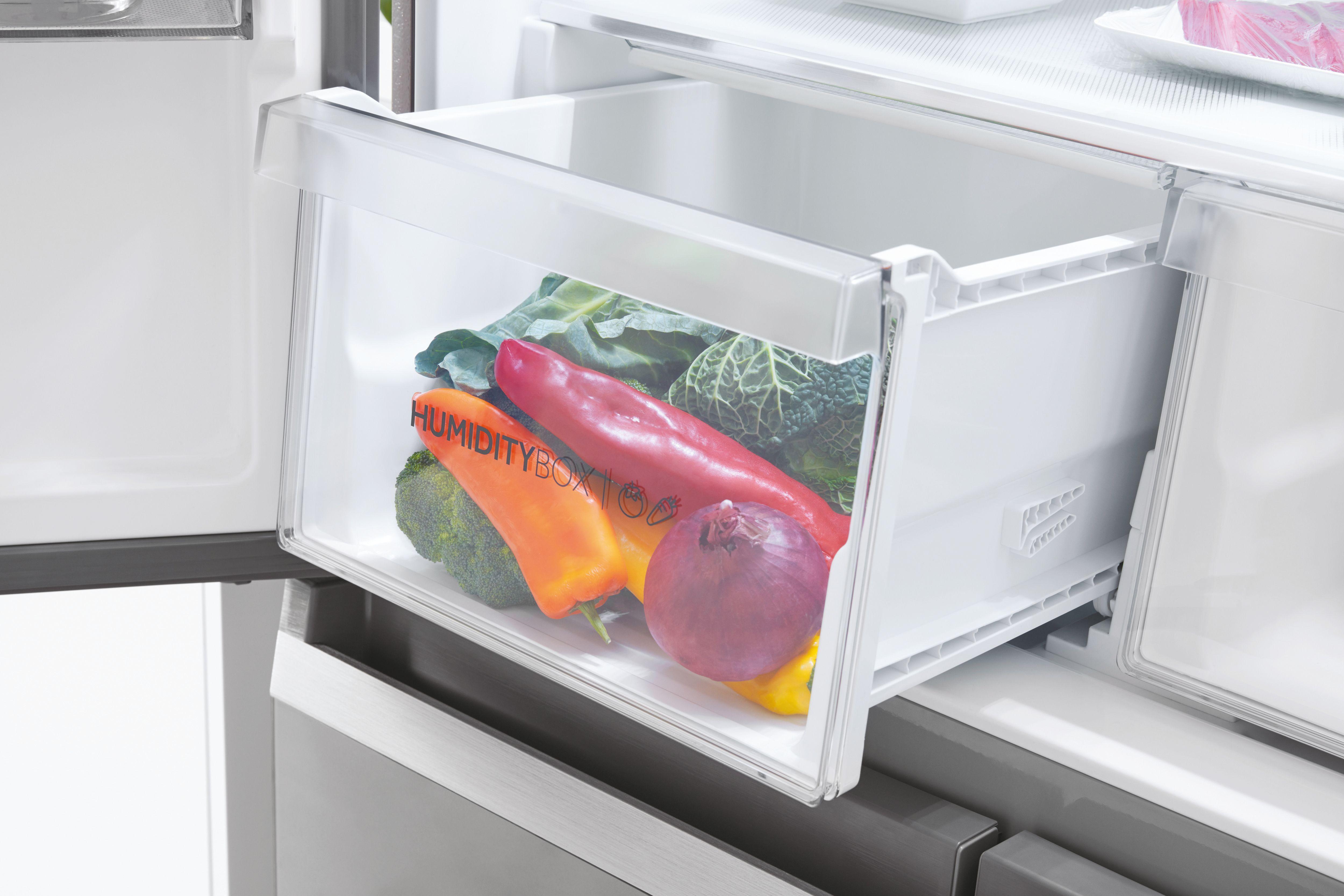 Cajón del refrigerador abierto, lleno de verduras como pimientos, brócoli y cebolla.