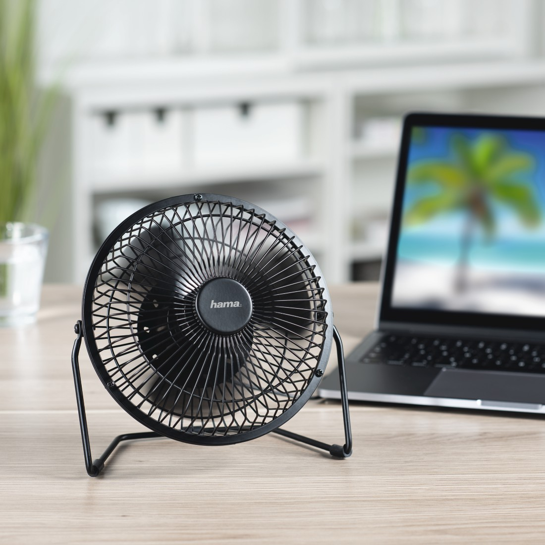 Ventilateur de bureau noir sur un bureau avec un ordinateur portable affichant une image de plage.