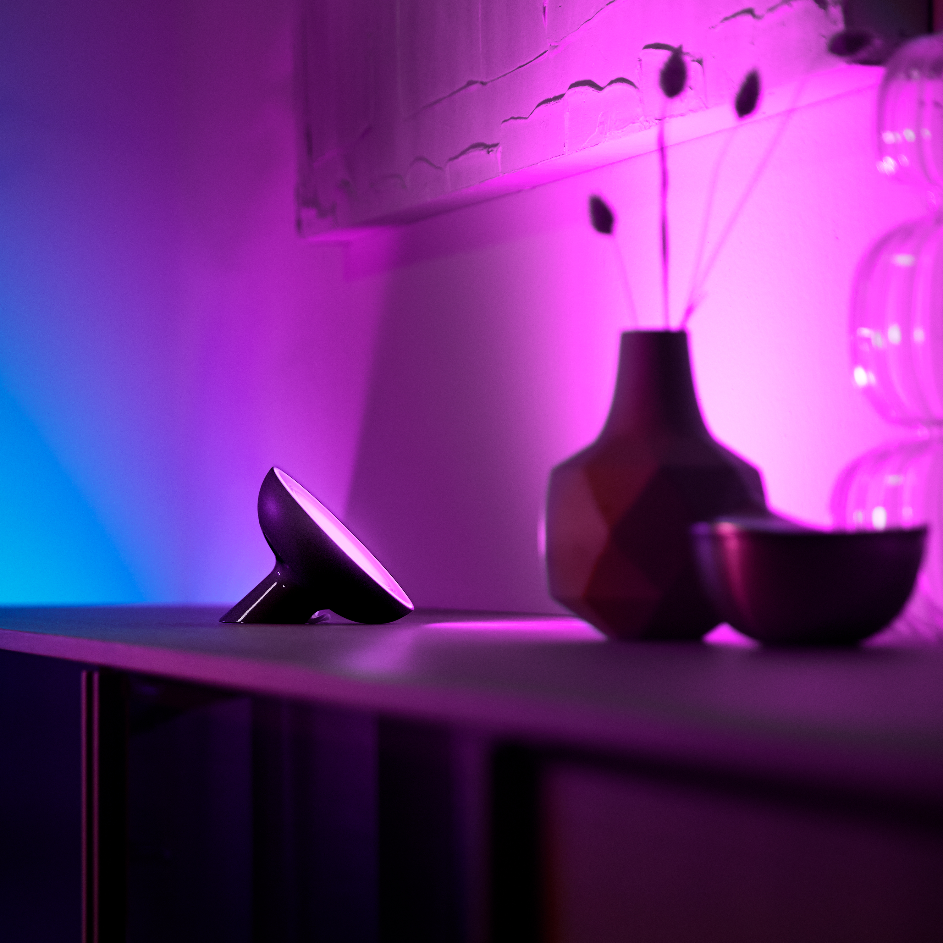 Black lamp with a purple and blue color gradient, next to a vase and bowl.
