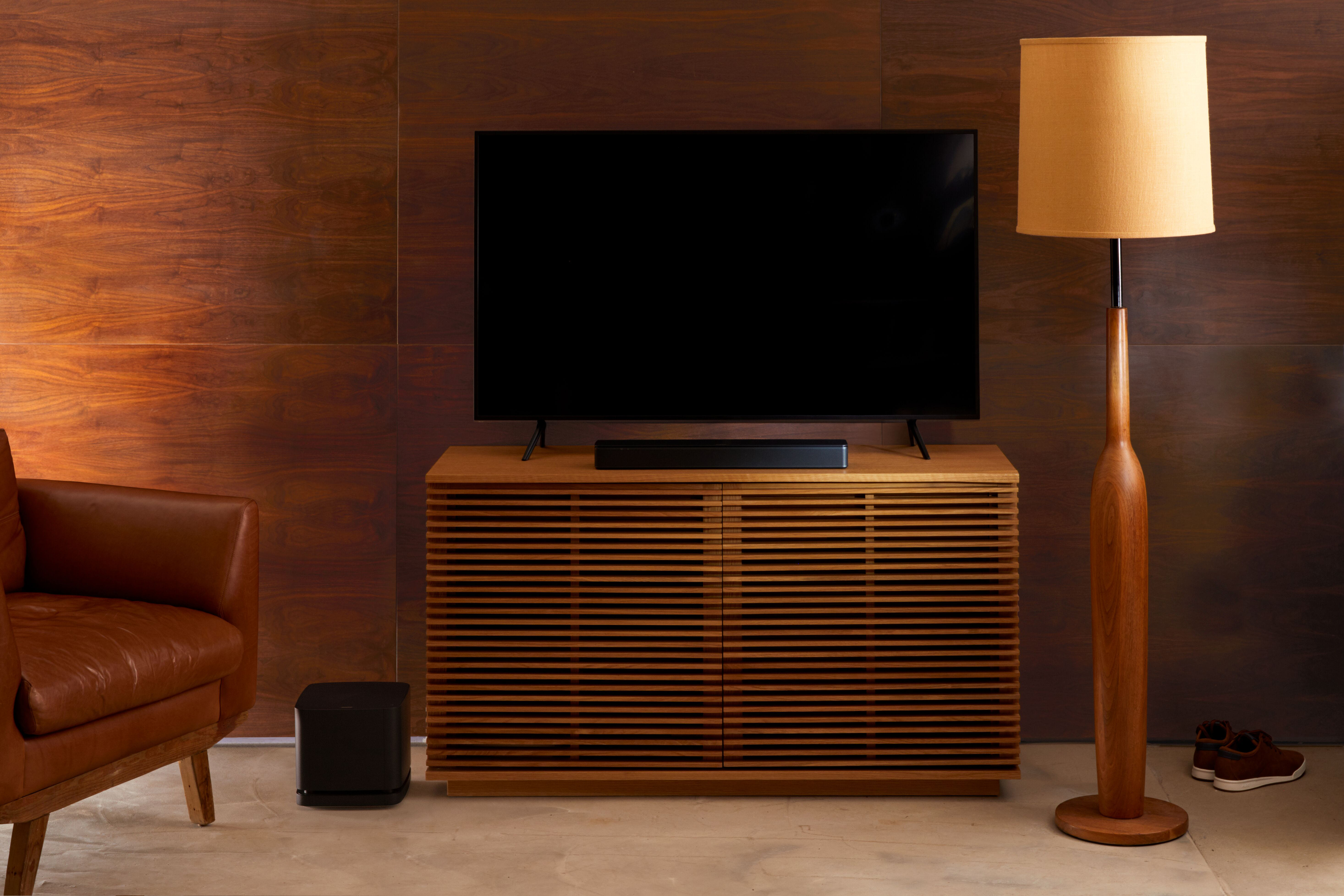 Wohnzimmer: Fernseher auf Holzschrank, Lampe, Ledersessel, dunkle Holzwand.