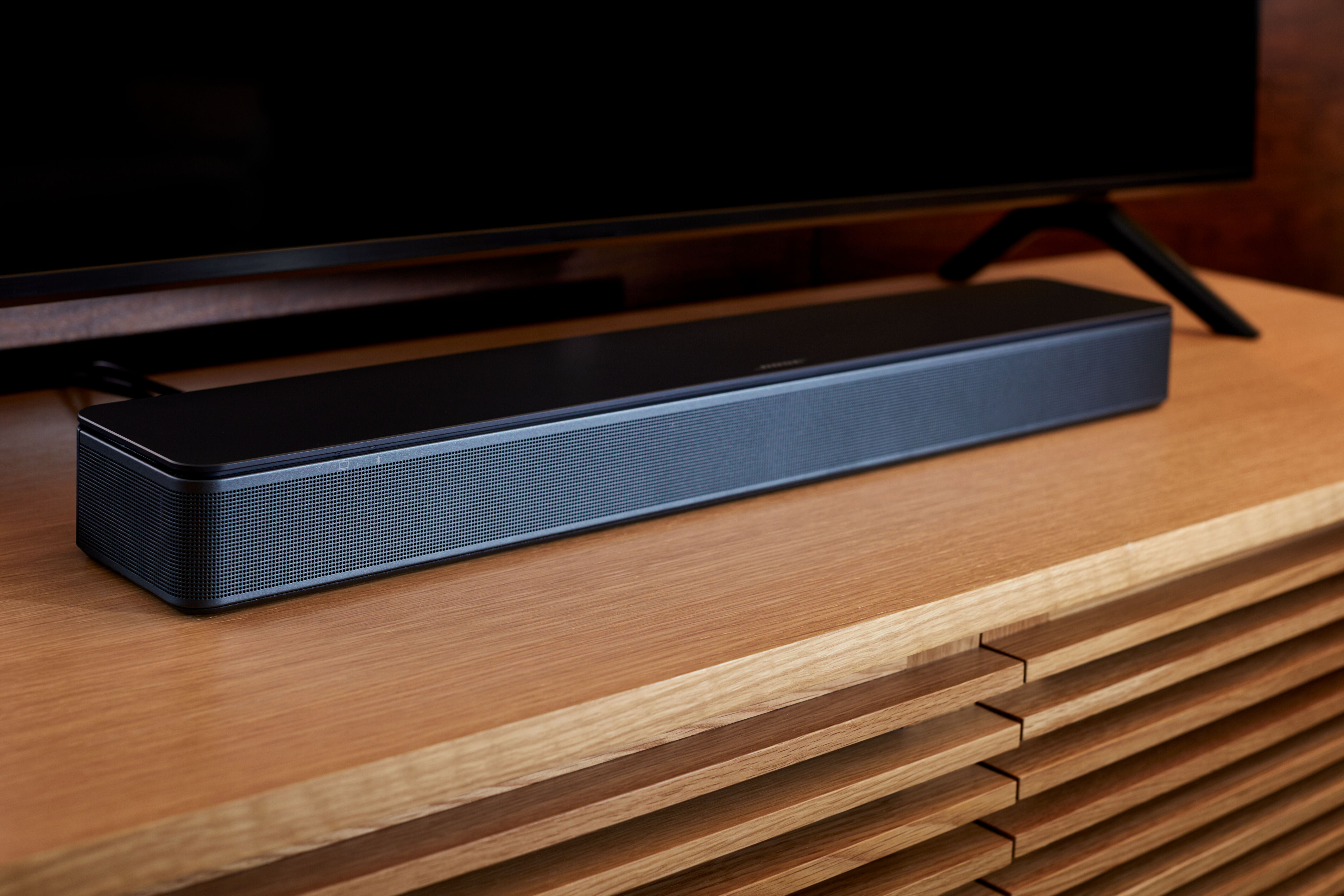Eine schwarze Bose Soundbar auf einem Holzschrank, mit einem schwarzen Fernseher darüber.