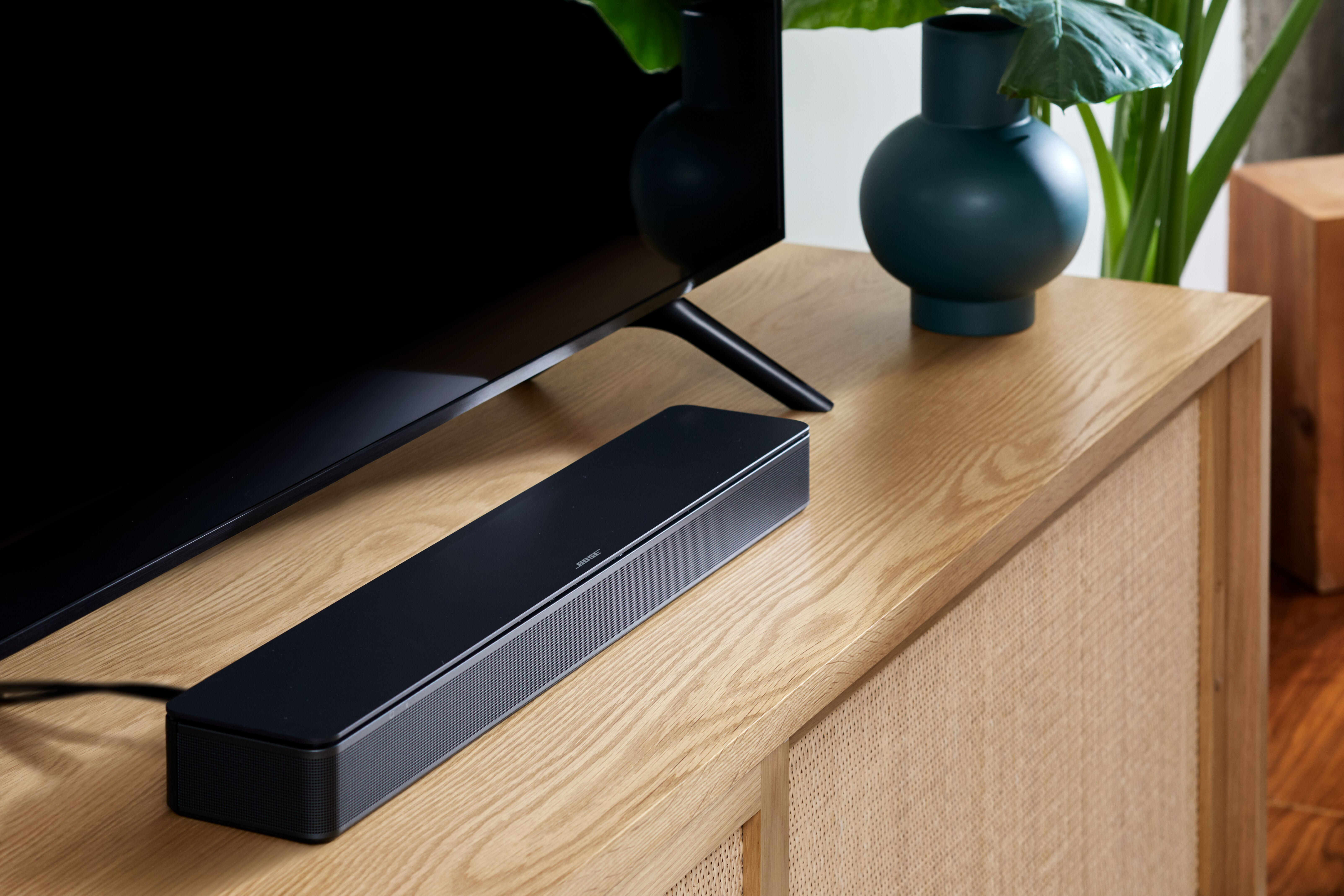 Eine schwarze Soundbar auf einem Holzschrank, mit einem Fernseher im Hintergrund. Der Raum ist modern.